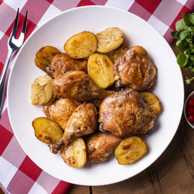 Tavuk parçalanmış, patates ve soğanlı, beyaz bir tabakta.