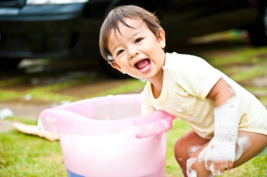 Babası arka planda arabayı yıkarken küçük kız köpükle eğleniyor. Yaz eğlencesi. Gülümseyen çocuk. Seçici odak.