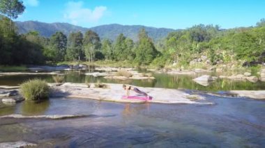 Havadan görünümü ışık saçlı kız huzurlu nehir kayaların arasında akış karşı yoga poz geçiyoruz Dandasana tutar