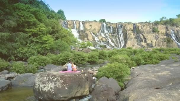 Camera beweegt langs man meisje zit op steen naar waterval — Stockvideo