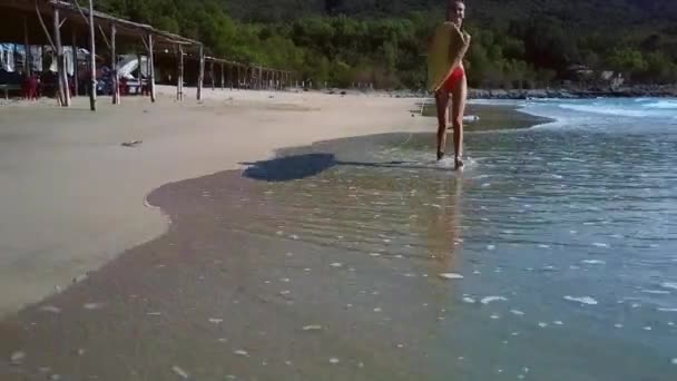 Ragazza cammina lungo la costa legata alla tavola da surf contro le piante — Video Stock