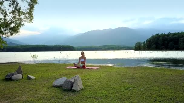 Flickan Sitter Matta Yoga Pose Lotus Framför Några Stenar Sjön — Stockvideo