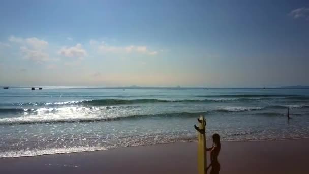 无人机视图妇女剪影举行板站立在海滩反对波光粼粼的太阳射线在海浪 — 图库视频影像