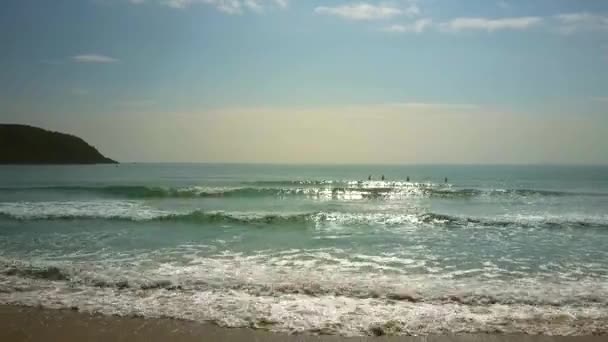 在无尽的蓝天下 美丽无垠的海浪在沙滩上翻滚 远方的冲浪者身影在地平线上 — 图库视频影像