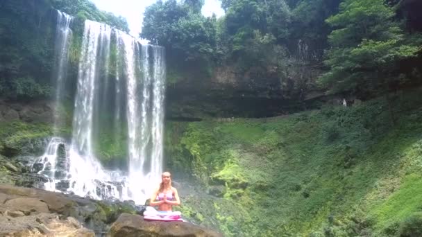 Flycam 示しています多くのストリームを持つ美しい泡滝と岩の上のロータスのポーズでリラックスする女の子 — ストック動画