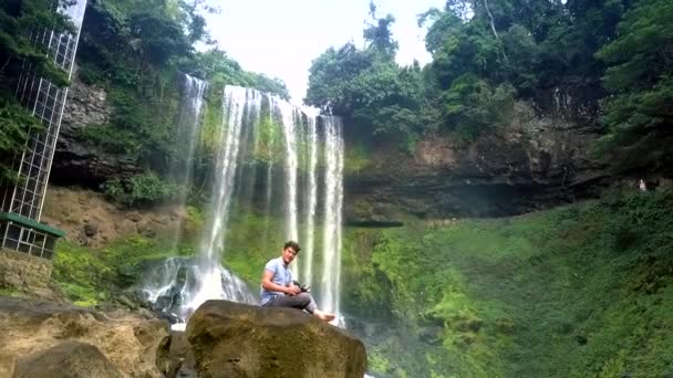 Moreno Sienta Roca Marrón Contra Cascada Pictórica Parque — Vídeos de Stock