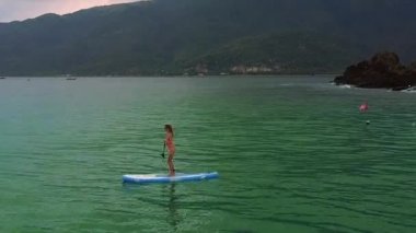 Sabahın erken saatlerinde karanlık engebeli sahil karşı yelken paddleboard üzerinde harika üst resim kız kırmızı bikini duruyor