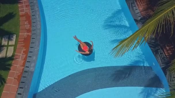 前景にプールやヤシの木の枝でインフレータブル リングで泳いでいる少女へカメラが動く — ストック動画