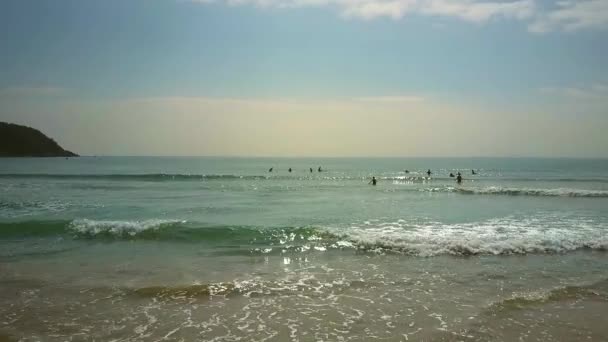 Olas del océano crach suavemente arena y surfistas distantes — Vídeo de stock