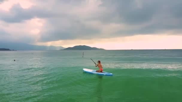 摄影全景苗条的女孩在红色比基尼游泳坐在 Paddleboard 之间蔚蓝的海洋到丘陵海滩 — 图库视频影像