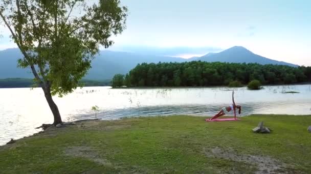 ピンクのマットの上の女の子が素敵な湖に対してポーズを保持します。 — ストック動画