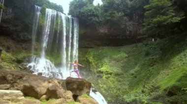 drone yaklaşımlar sarışın Bayan yoga konumda duvara çıplak kayaların üzerinde düşen su parkı ayakta