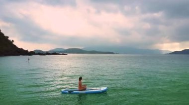 sürüklenir pembe güneş doğarken kırmızı bikini egzotik üst resim kız ilginç yoga poz yarım Lotus paddleboard turkuaz Okyanusu üzerinde