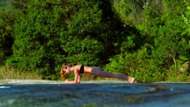 Genç kadın dere kıyısında yoga yapıyor. 