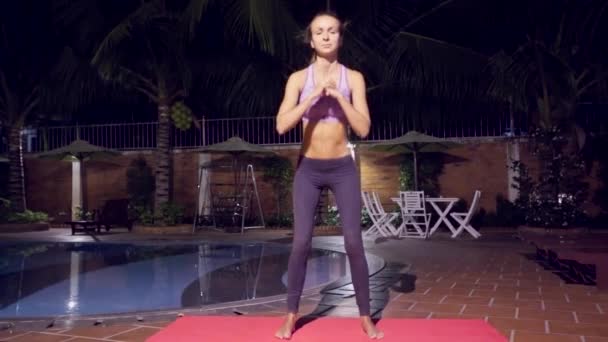Симпатичная девушка занимается фитнесом у бассейна по вечерам — стоковое видео