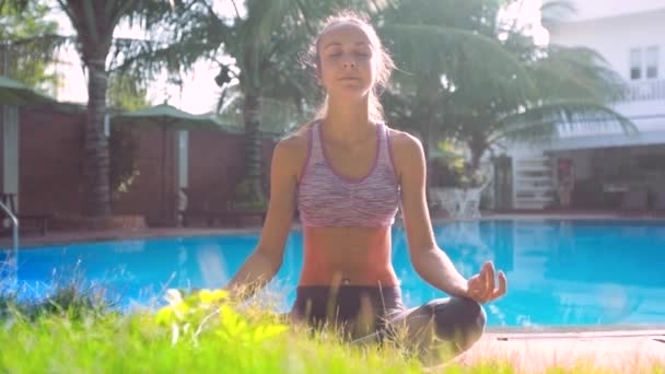 Söt flicka sitter i yoga posera Lotus mot pool palms hotel — Stockvideo
