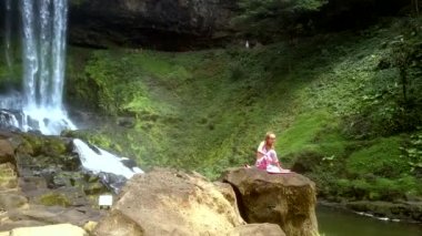 Bayan kaya şelale tarafından yoga konum değiştirme oturur