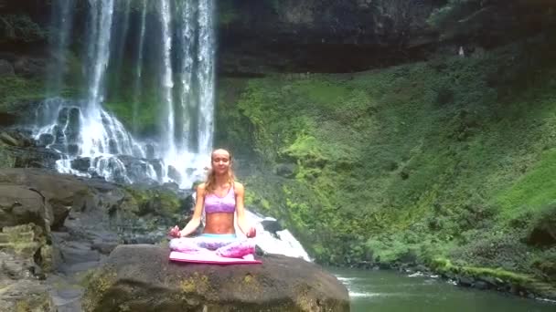 Леди медитирует в позе лотоса против пенного водопада — стоковое видео