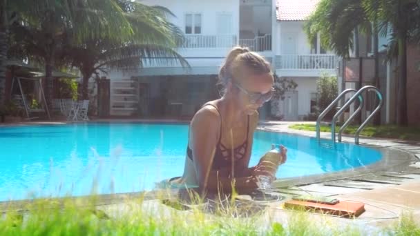 Fille prend bouteille d'eau et boissons appuyé sur la barrière de la piscine — Video
