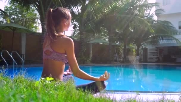 Zonnestralen licht meisje ontspannen in pose Lotus door kant uitzicht op het zwembad — Stockvideo