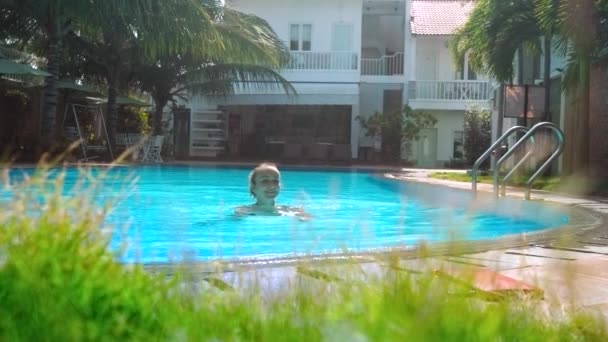 Дівчина плаває через готельний басейн до бар'єру серед долонь — стокове відео