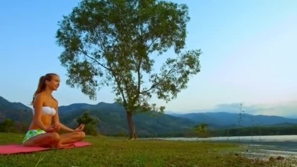 Štíhlá dívka spočívá v póze Lotus podivné osamělý strom na kopce — Stock video