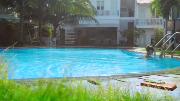 Smal tjej i bikini kommer ur hotellets pool på Metall trappor — Stockvideo