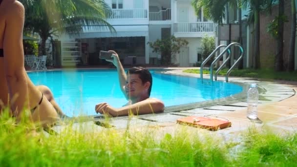 Guy bilder slim flicka i bikini som sitter på pool barriär — Stockvideo