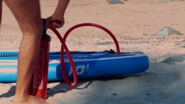 Låg vinkel skott kille blåses paddle board med pump på benet — Stockvideo
