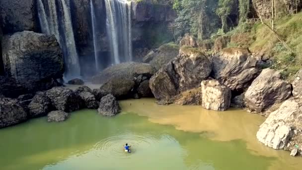 Junge schwimmt in Fluss mit felsigem Ufer bei Wasserfall