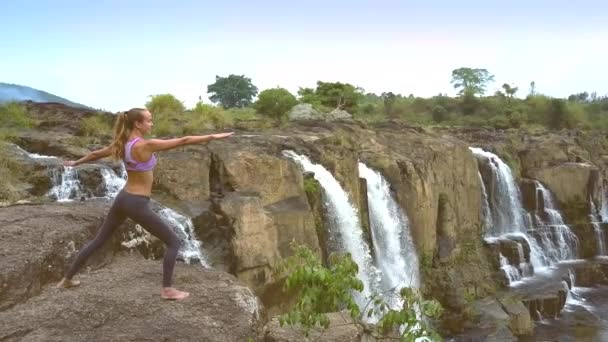 Drone verwijderd meisje yoga houding door waterfall wijzigen — Stockvideo