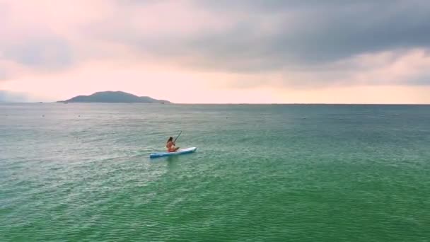 Lady swims sitting on paddleboard in calm ocean at sunrise — Stock Video