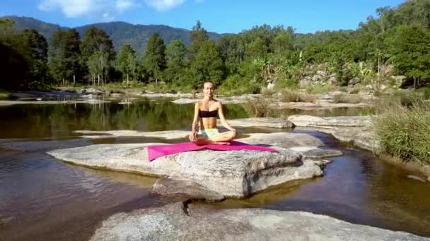 Chica se sienta en la posición de yoga en piedra contra el río tranquilo — Vídeo de stock