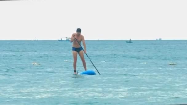 Strong guy approaches beach sailing on paddle board — Stock Video