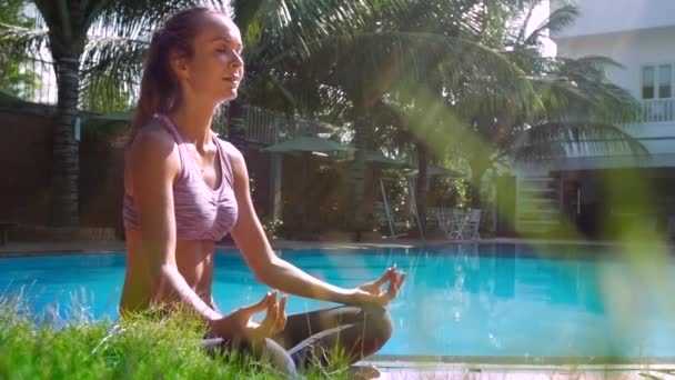 Söt flicka sitter i Lotus pose att sätta händerna på knäna av poolen — Stockvideo