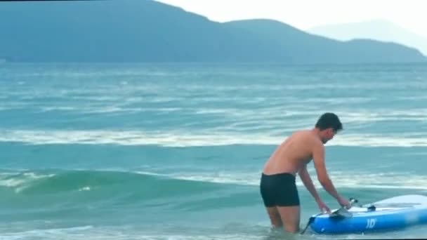 Homme se tient dans l'eau obtient sur la planche à pagaie contre les collines — Video