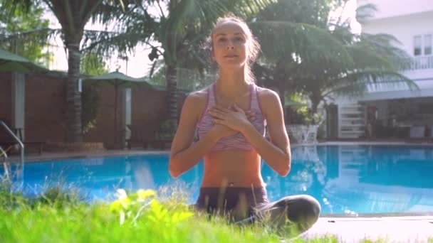 Fille dans la pose de yoga Lotus avec les mains sur la poitrine se détend près de la piscine — Video