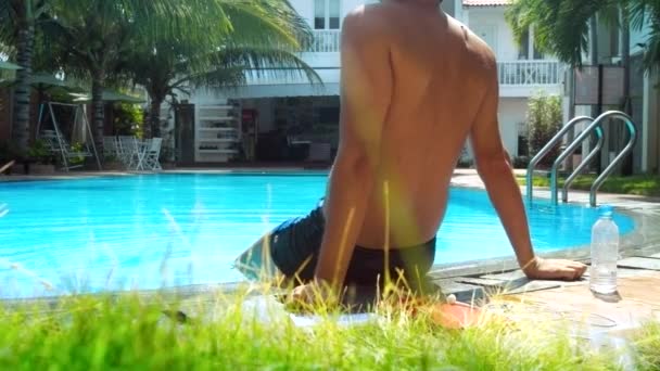 Задняя сторона сильный мужчина с загорелой спиной сидит на барьере бассейна — стоковое видео