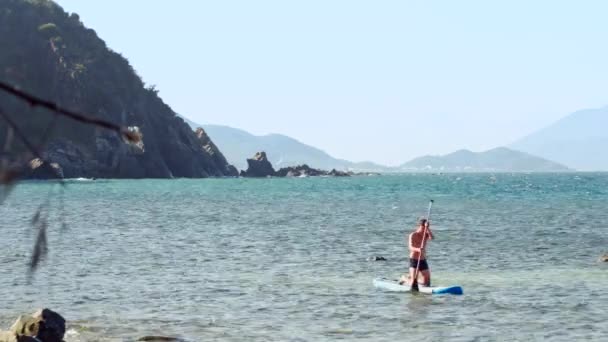 Facet podchodzi ocean plaża kucanie na paddleboard — Wideo stockowe