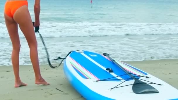 Low angle shot girl takes paddle board leash and fastens — Stock Video