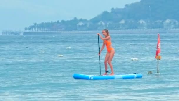 Girl paddles SUP board past hilly beach in haze — Stock Video