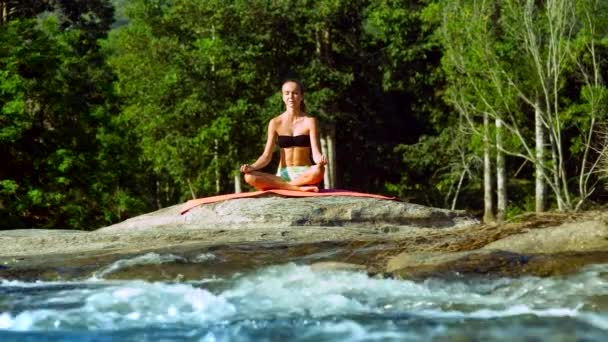 Menina magro medita em ioga pose Lotus por rio com corredeiras — Vídeo de Stock