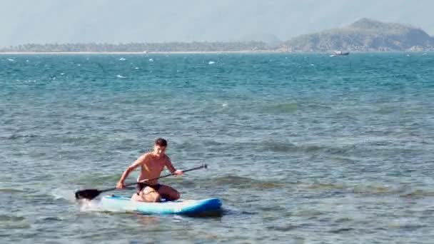 Hombre fuerte se sienta en el paddleboard flotando en mar abierto — Vídeos de Stock