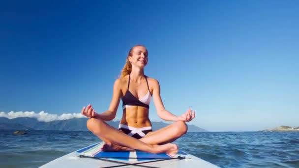 Дівчина в позі Lotus посміхається на дошці весла серед океану — стокове відео