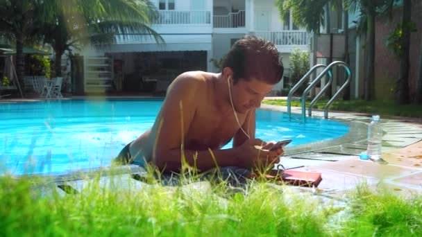 Guy dinglar fötter i poolvattnet surfa internet telefon — Stockvideo