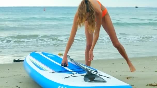 Стройная блондинка берет резиновую доску прогулки к океану — стоковое видео