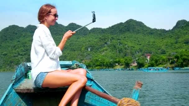 Blond woman makes selfie sailing on boat past hilly bank — Stock Video