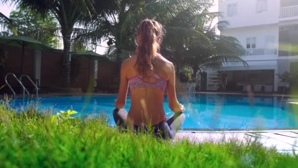 Grama verde e menina relaxa em pose Lotus por piscina vista traseira — Vídeo de Stock