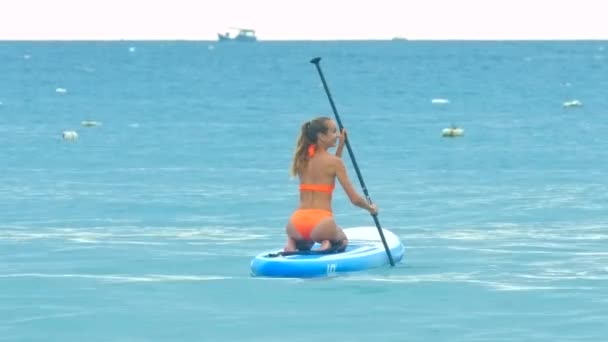 Baksidan Blond Flicka Med Hästsvans Orange Bikini Paddlar Styrelse Sitter — Stockvideo