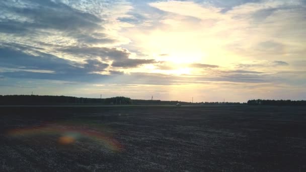 Solnedgången solen bakom molnen ovanför mörka fält och road — Stockvideo